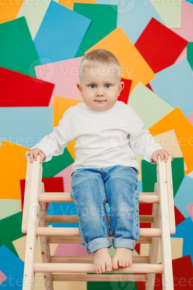 In a vibrant studio full of colors and textures, a lively toddler joyfully posed on a whimsical ladder, creating a unique artistic backdrop for this heartwarming moment of childhood joy photo