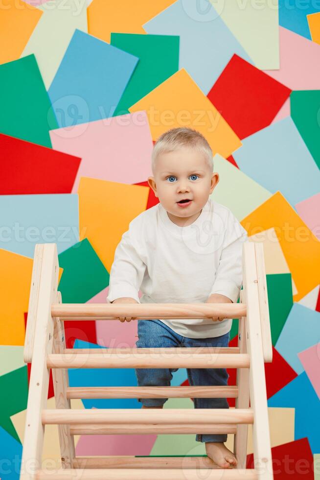 An adorable and energetic toddler is joyfully climbing a wooden structure, set against a vibrant and colorful background that adds to the cheerful atmosphere of play and exploration photo