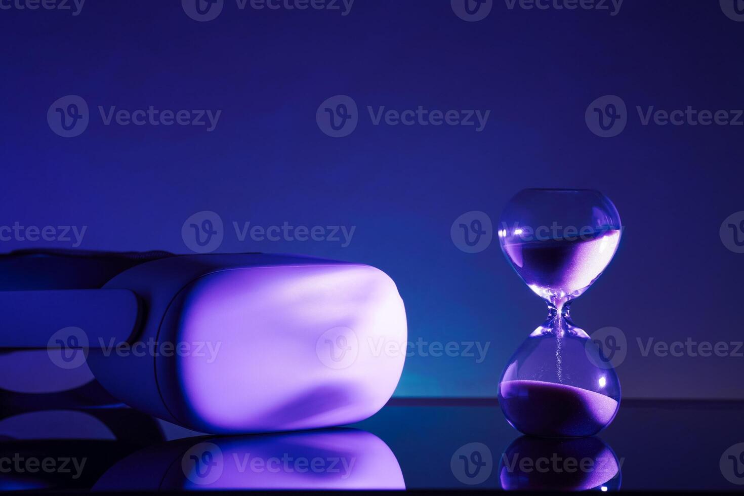 Creative composition featuring a glowing VR headset paired with an hourglass, symbolizing technology and time, on a textured blue backdrop. Perfect for tech, innovation, and timeless concept themes photo