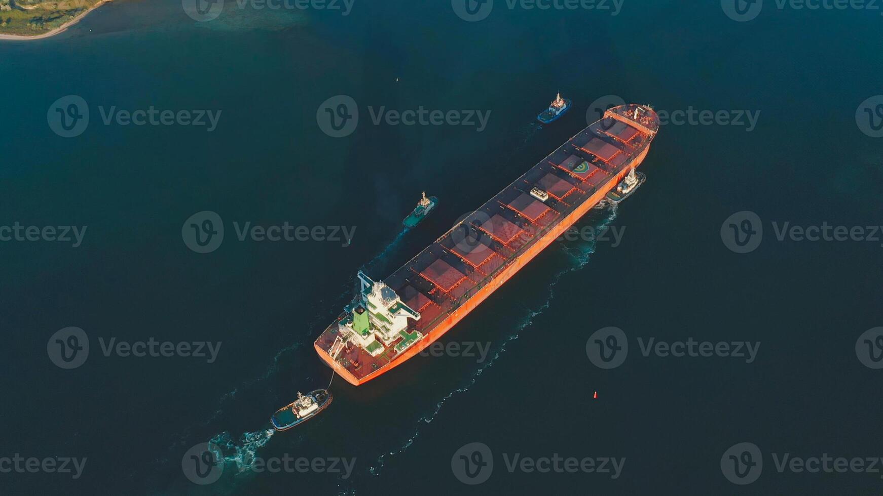 Aerial view of a large cargo ship being driven out of the harbor by four tugboats. photo