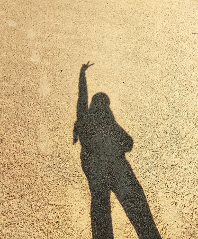 A shadow of a person standing on the beach with their hands up photo