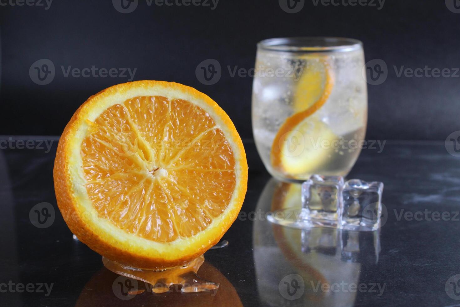 lemonade with orange and ice in glass on a black background next to lies ice and orange. Summer drink on a black background photo