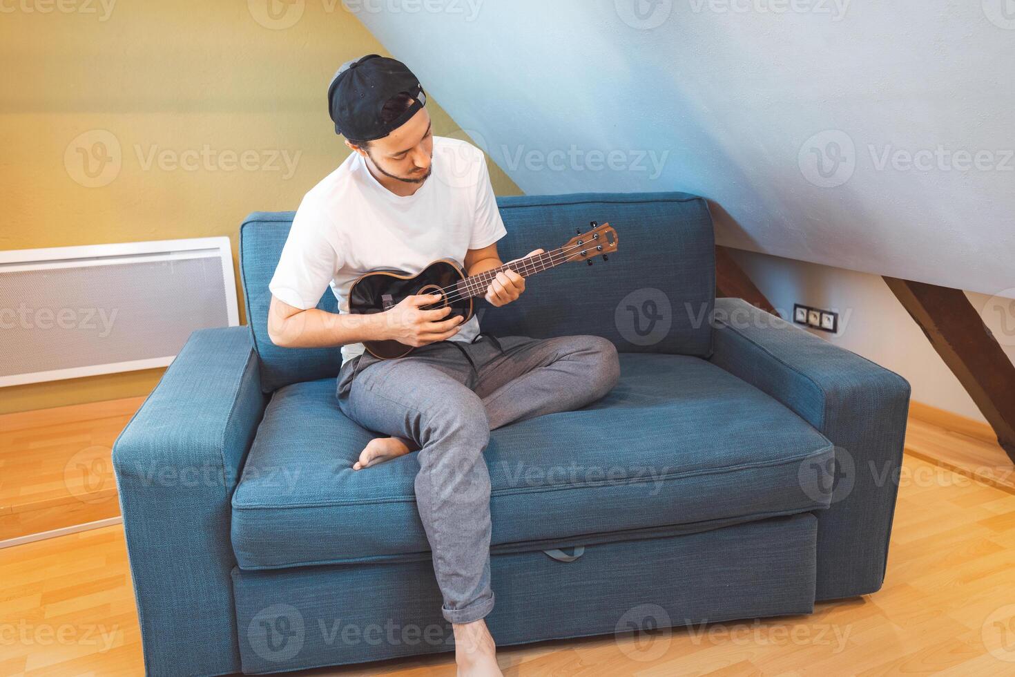 Relaxed guy sitting and playing ukulele by window photo