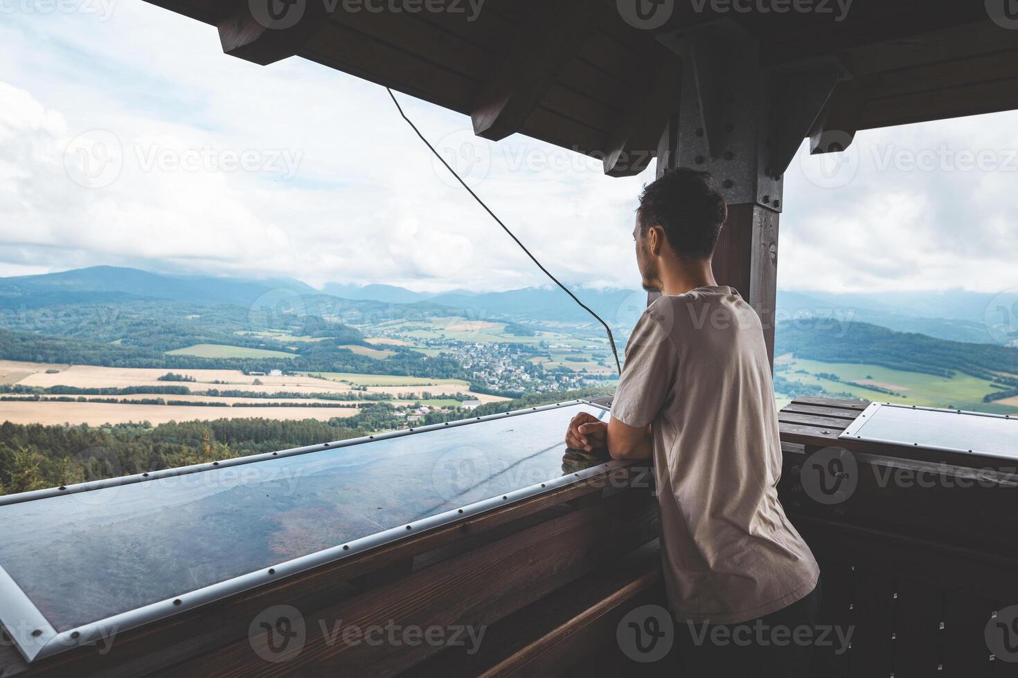 Man Finger points at a weathered orientation board on a viewing platform, labeling peaks of the Jeseniky Mountains unfolding across lush forested hills photo