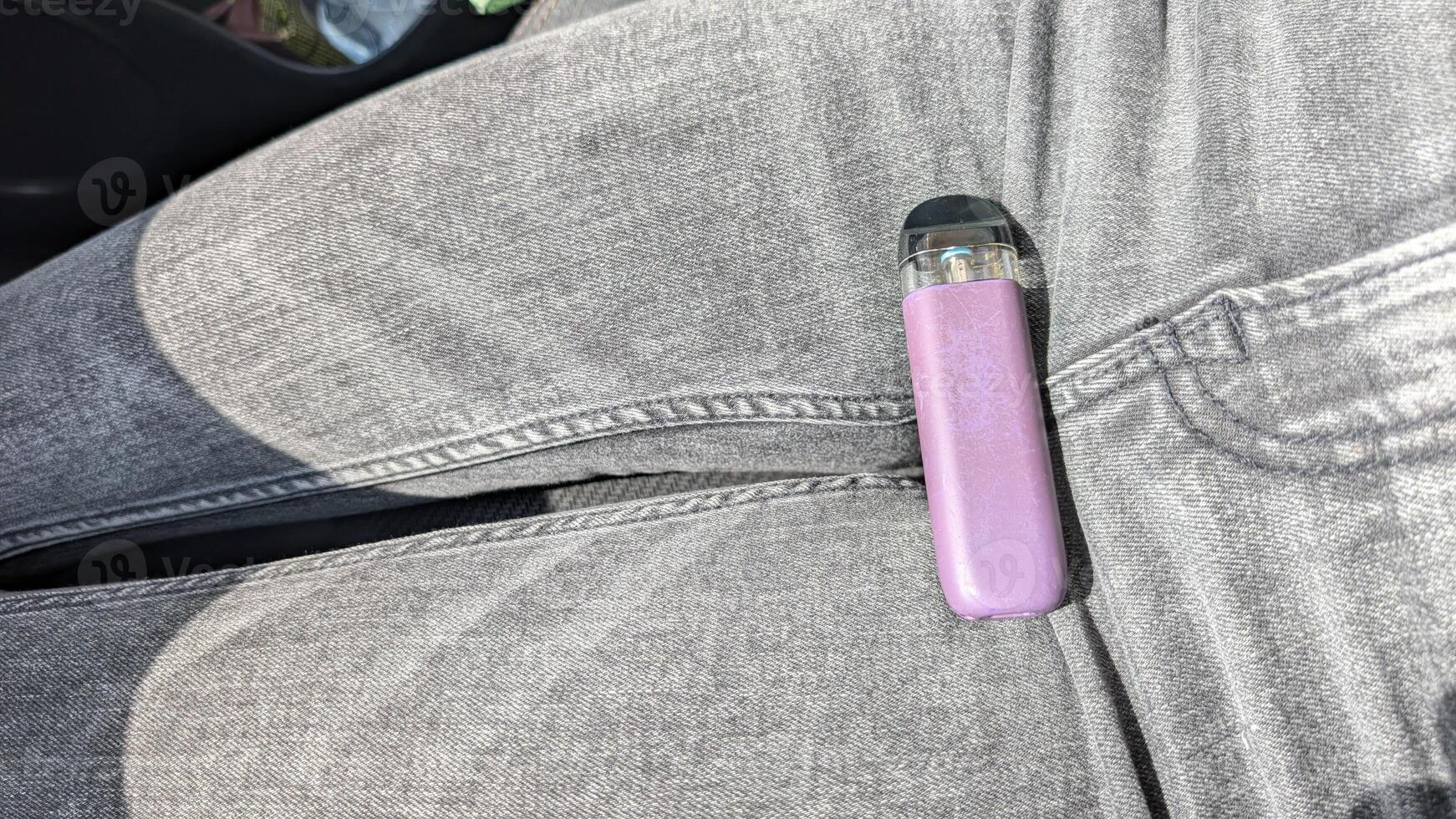 A Casual Vaping Moment A Trendy Vape Pen Resting Stylishly Upon a Pair of Jeans During Leisure Time photo