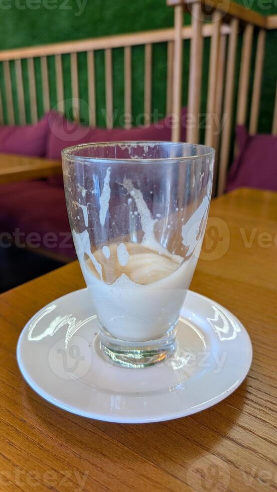 An Empty Glass with Milky Residue on a Plate Displayed in a Cozy and Inviting Cafe photo