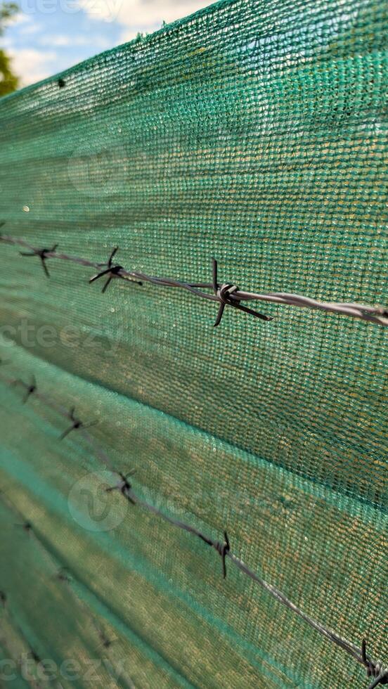 CloseUp Image of a Green Mesh Fence that Effectively Features Barbed Wire Along Its Top Edge photo