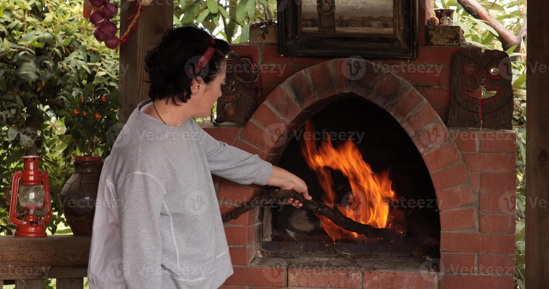 Outdoor oven in garden setting showcasing person adding wood to fire, creating vibrant flames and warmth, surrounded by natural scenery and rustic decorations which enhance outdoor cooking experience photo