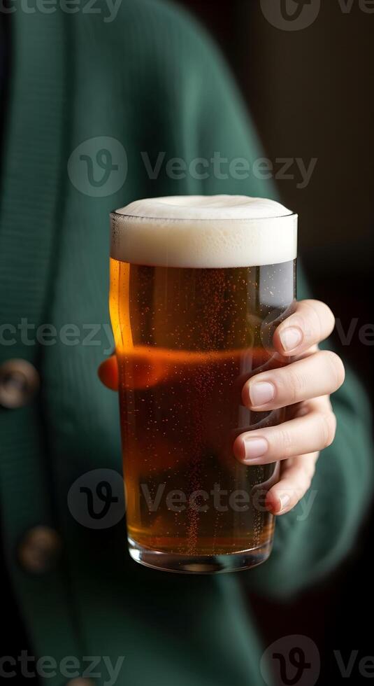 Female hand in green holds a glass of fresh light beer and extends it to the camera. Vertical template for St. Patrick's Day, beer parties, Oktoberfest and beer factory advertising with space for text photo