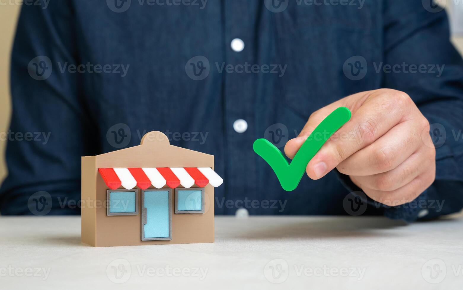 A man holds a green check mark near a store. Pass the test. Quality verification. Business permits. Successful inspection, business licensing, or compliance with regulations. Audit approval photo