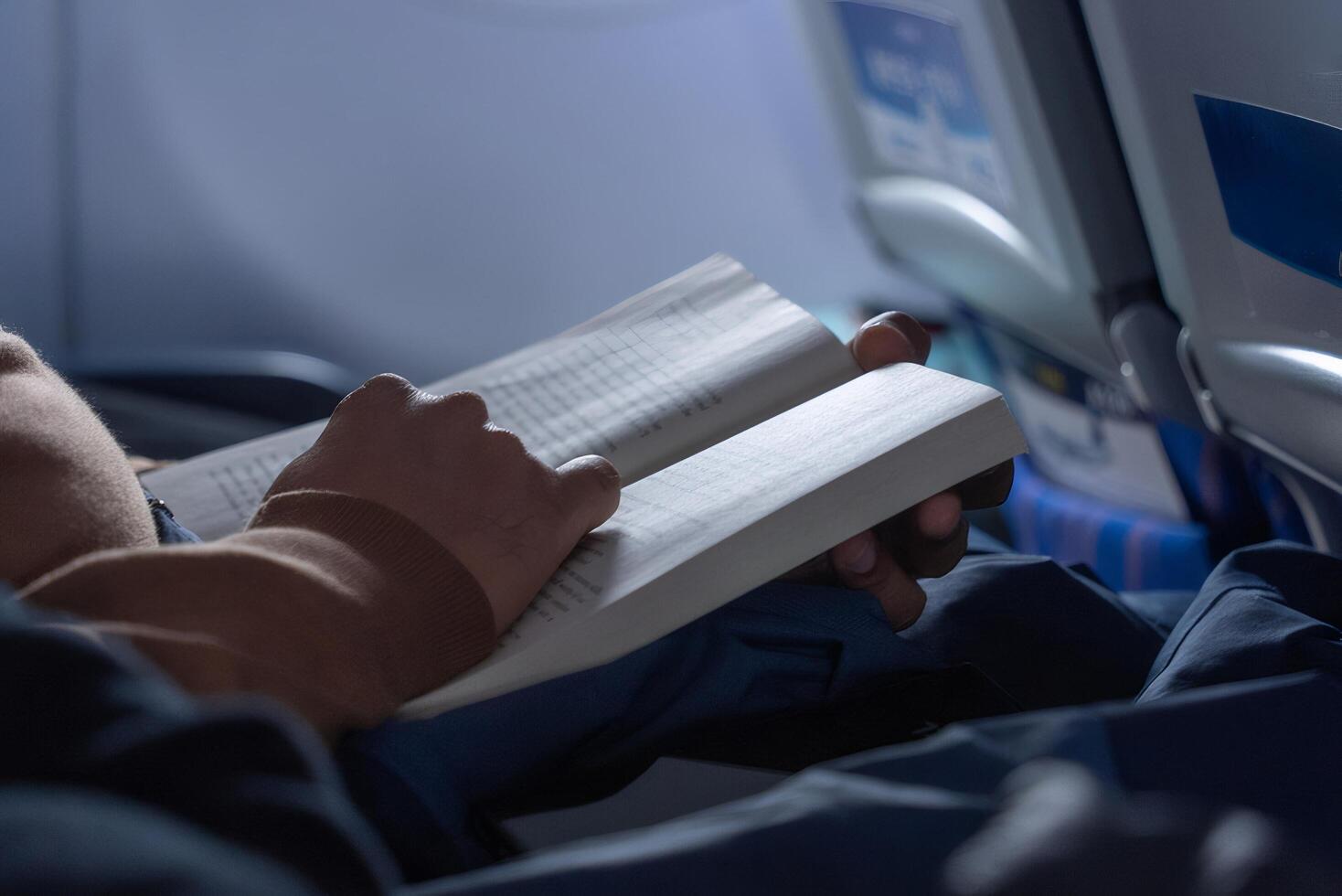 Person Reads Book Inside Airplane Cabin during Flight Under Dim Lighting photo