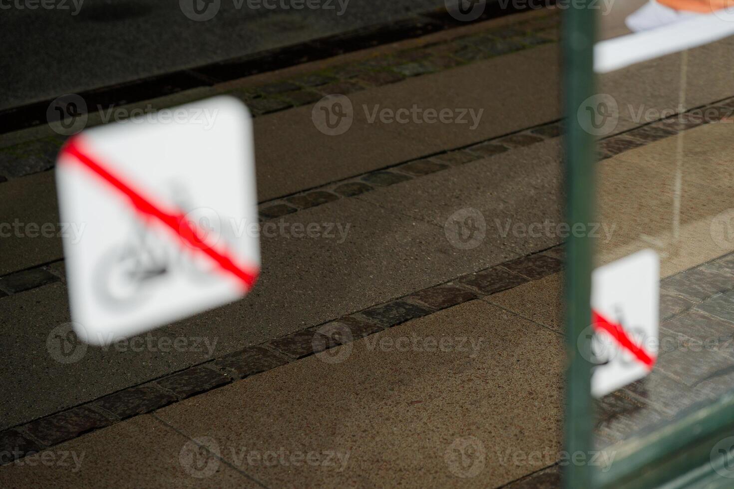 In the window is sign indicating that bicycles are prohibited, the sidewalk is reflected photo