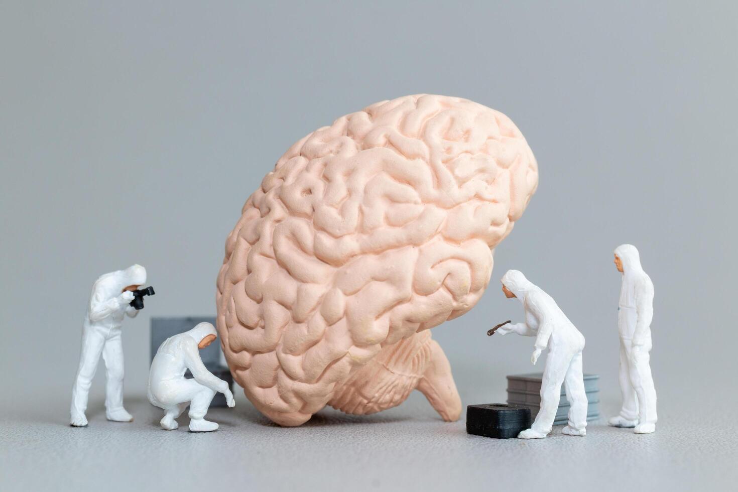 Miniature figures in hazmat suits inspect and analyze a giant brain model photo