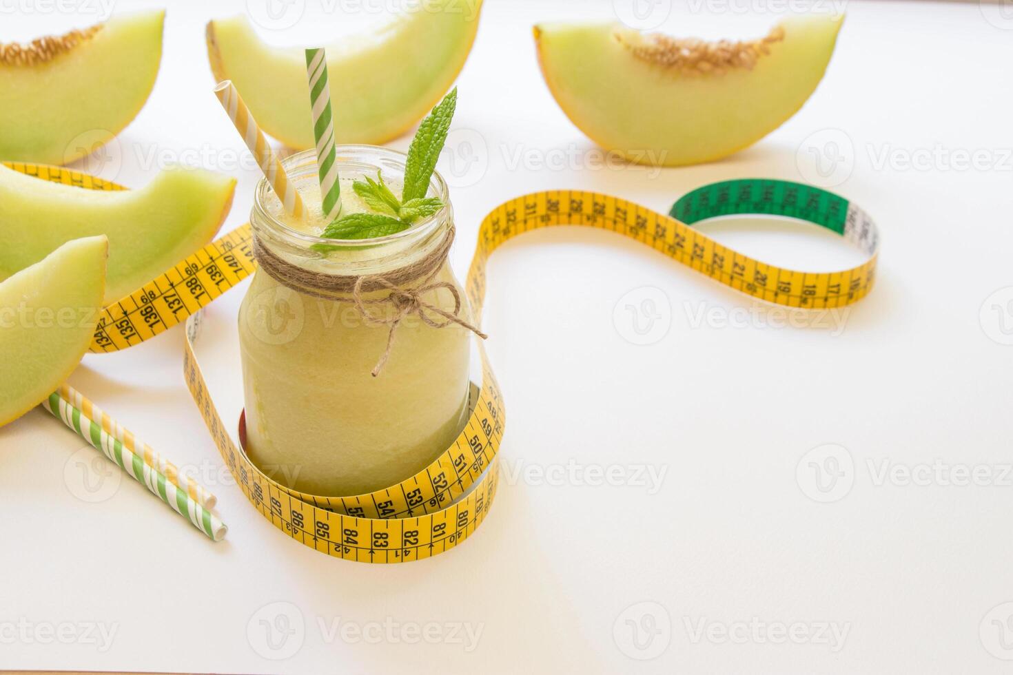Jar with melon smoothie near cut slices of melon, centimeter, straws right empty place for text on a white background. Melon smoothie in a jar. Horizontal. Daylight. photo