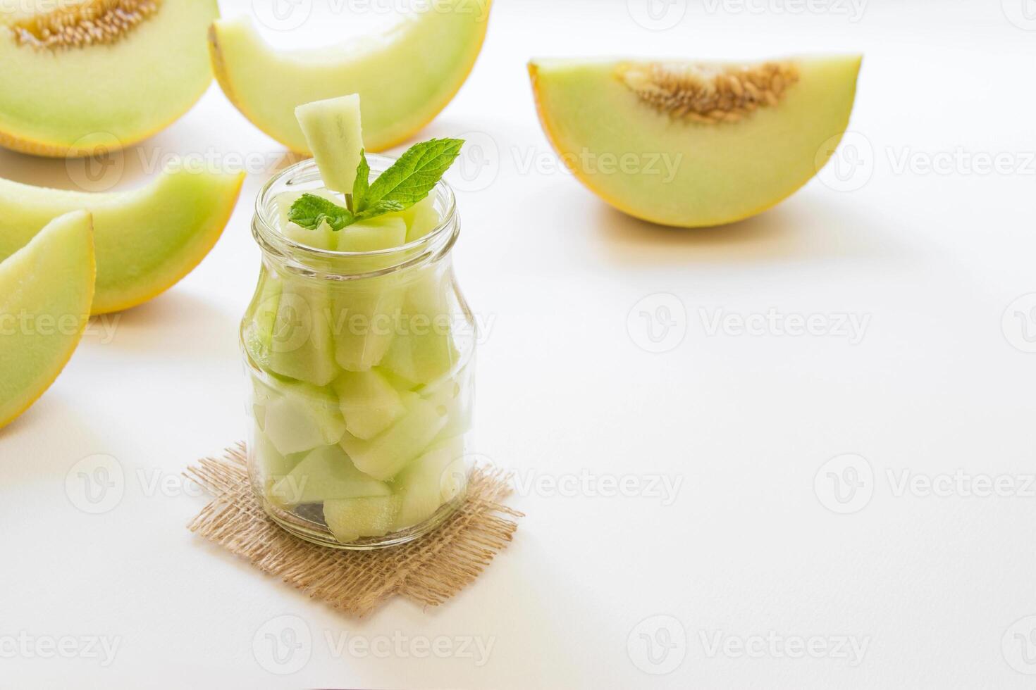 Glass jar with melon pieces on burlap napkin near cut slices of melon right empty place for text on a white background. Pieces of melon in a jar. Horizontal. Daylight. photo