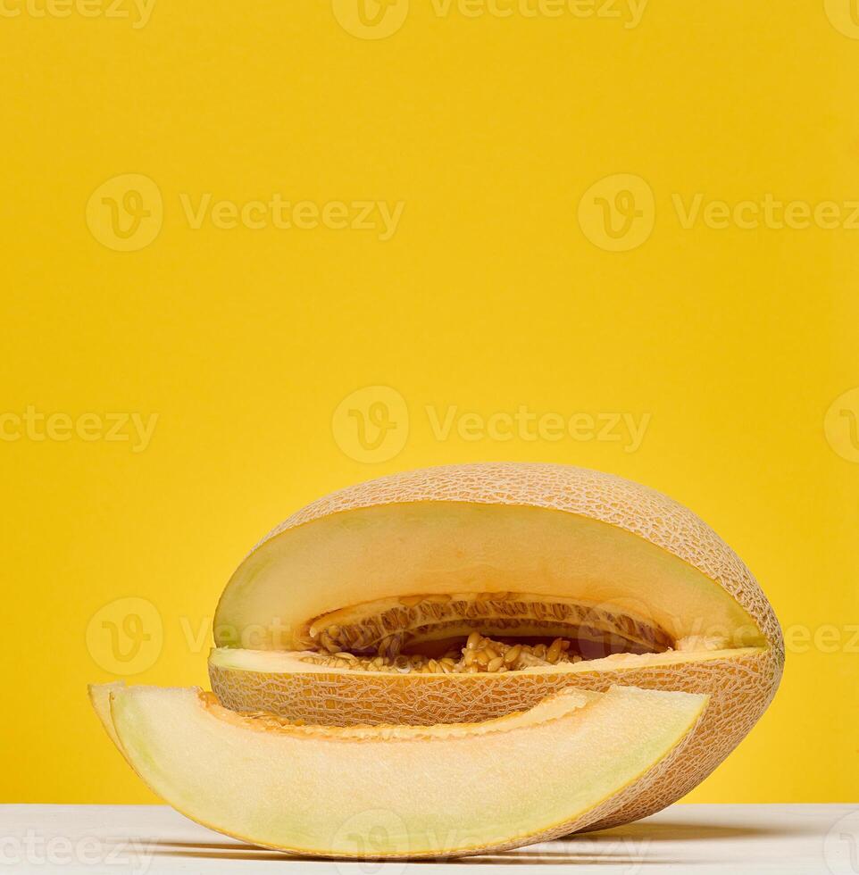 Half of a cantaloupe melon and a single slice placed on a white surface. Yellow background. photo