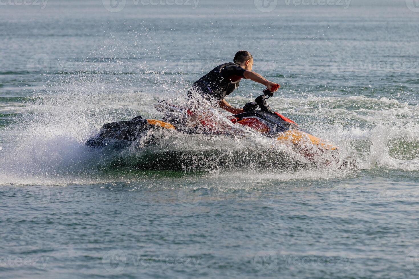 A young man zooms over sparkling water on a jet ski, the sun overhead and adrenaline rushing. photo