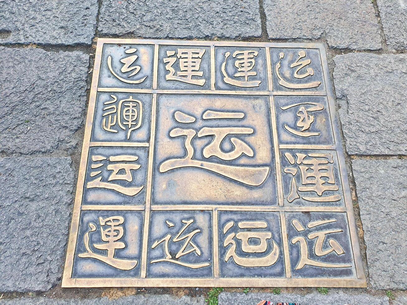 decorative bronze plaque with various Chinese characters is embedded in a stone pavement, showcasing calligraphy styles and symbols for Luck photo
