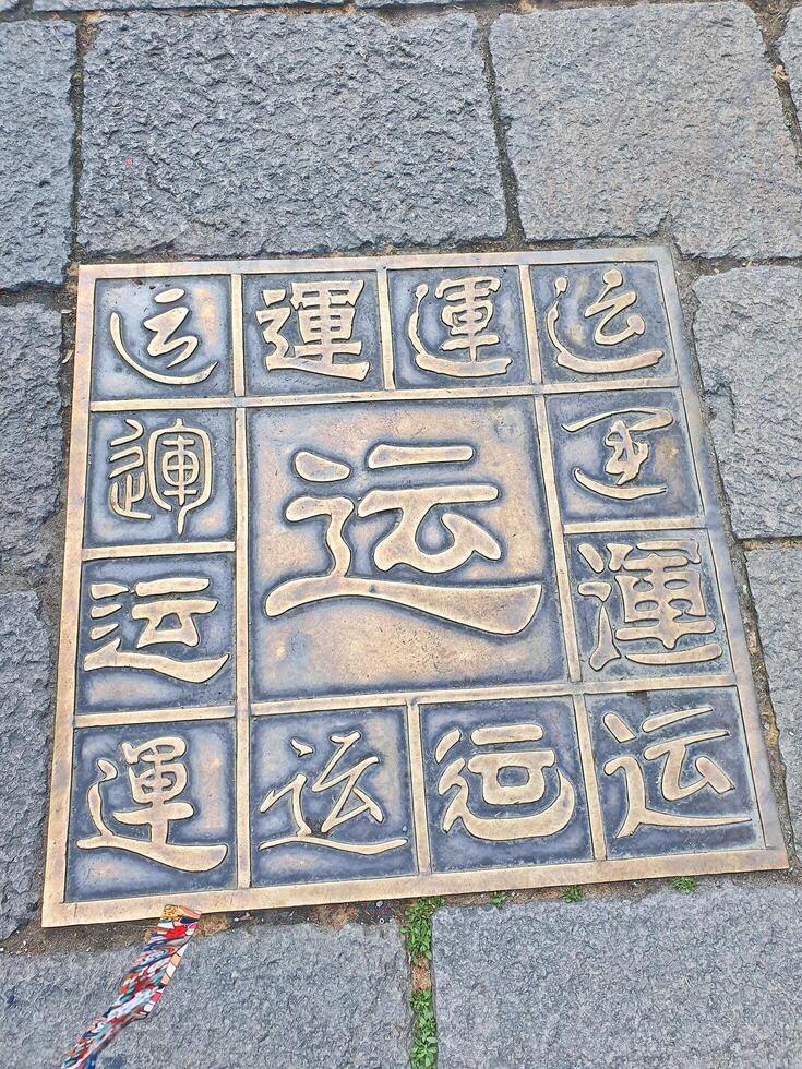 A decorative bronze plaque with various Chinese characters is embedded in a stone pavement, showcasing calligraphy styles and symbols for Luck photo