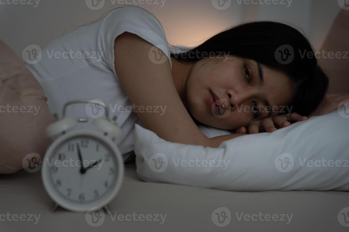 asian woman in bed late trying to sleep suffering insomnia, sleepless or scared in a nightmare, looking sad worried and stressed. Tired and headache or migraine waking up in the middle of the night,. photo