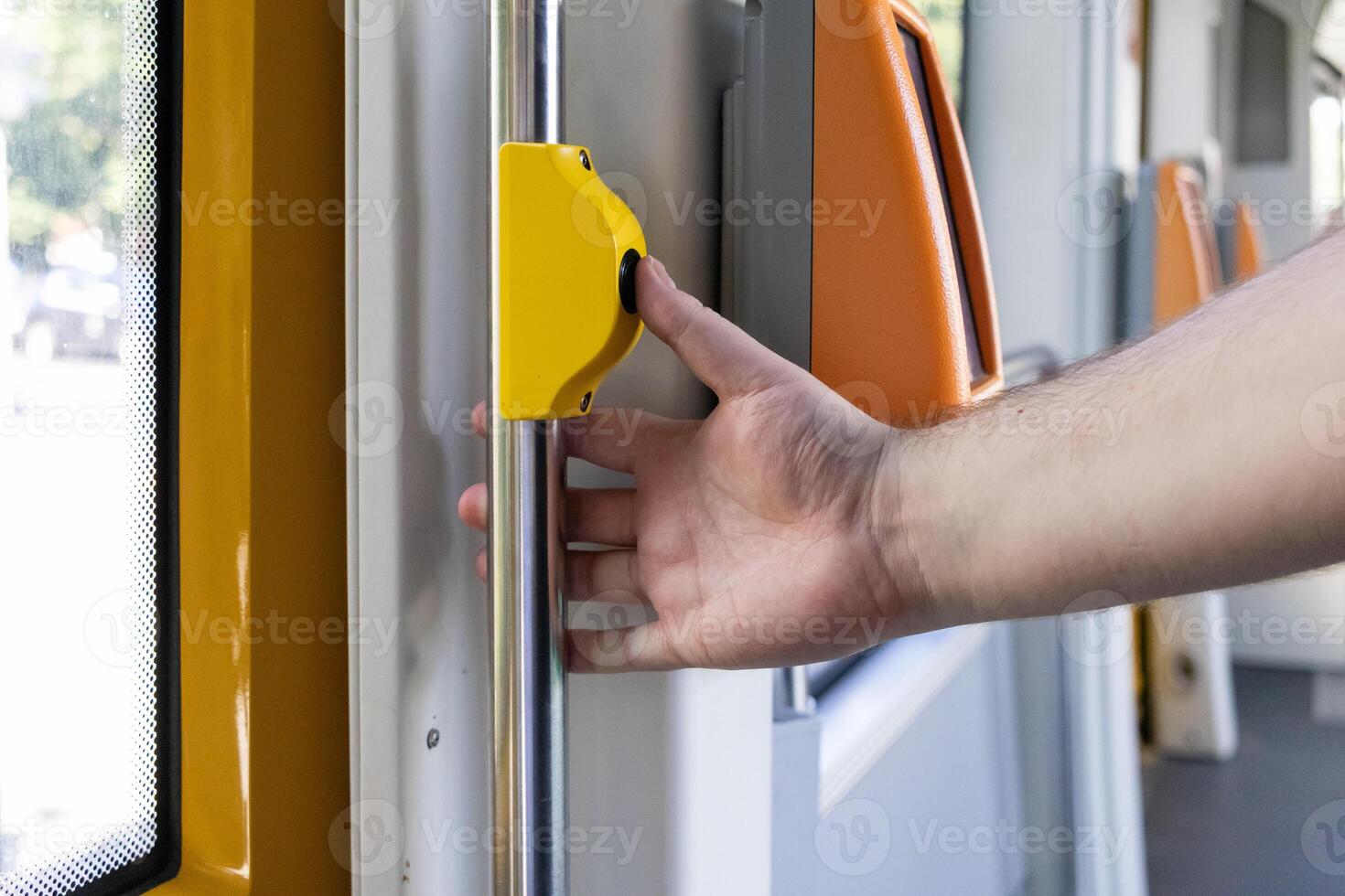 Hand pressing an essential yellow stop request button inside a modern public transport vehicle, indicating passenger's desire to exit at the next station photo