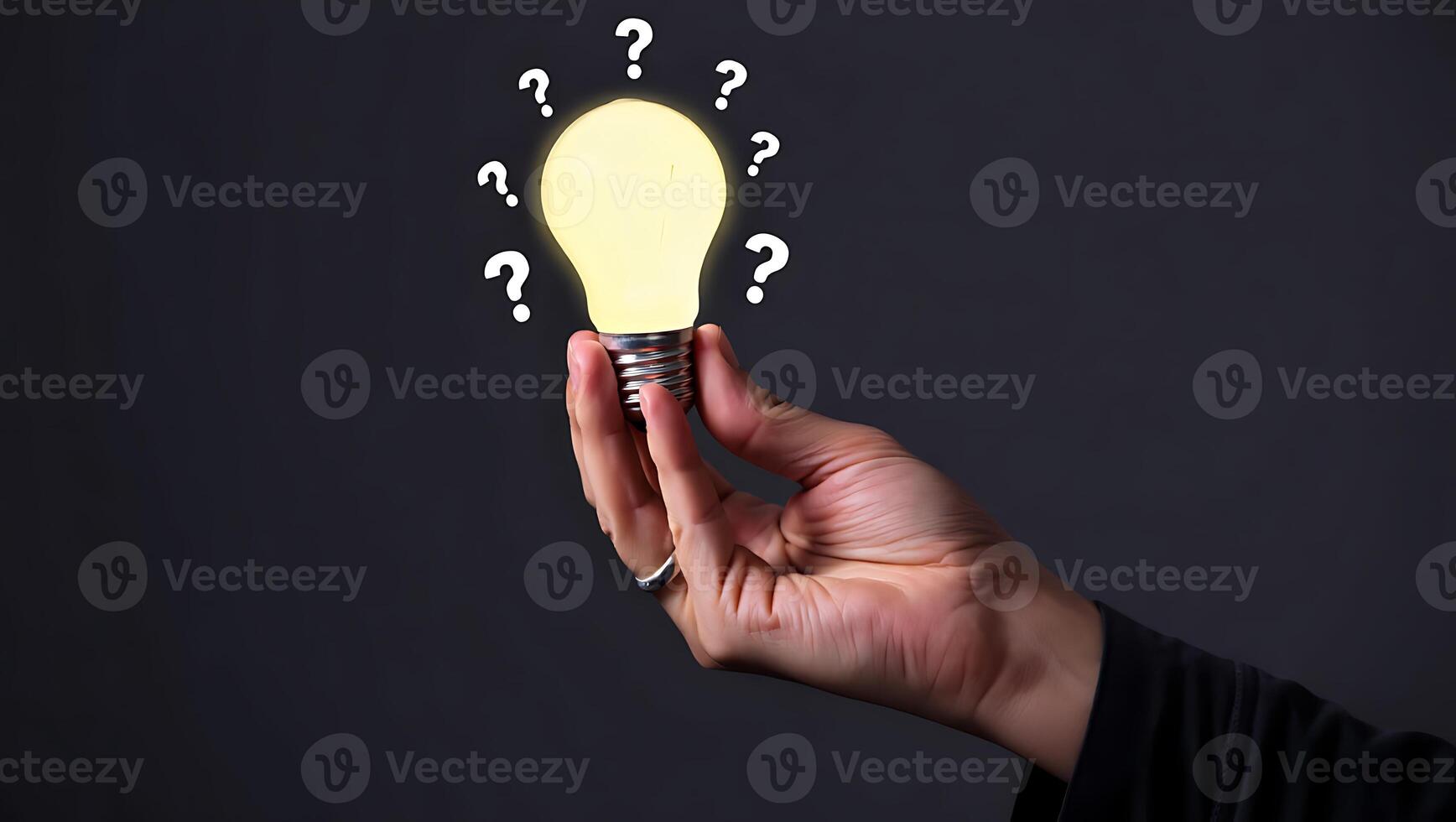 Hand Holding a Glowing Light Bulb Surrounded by Question Marks on Dark Background Conceptual Image photo