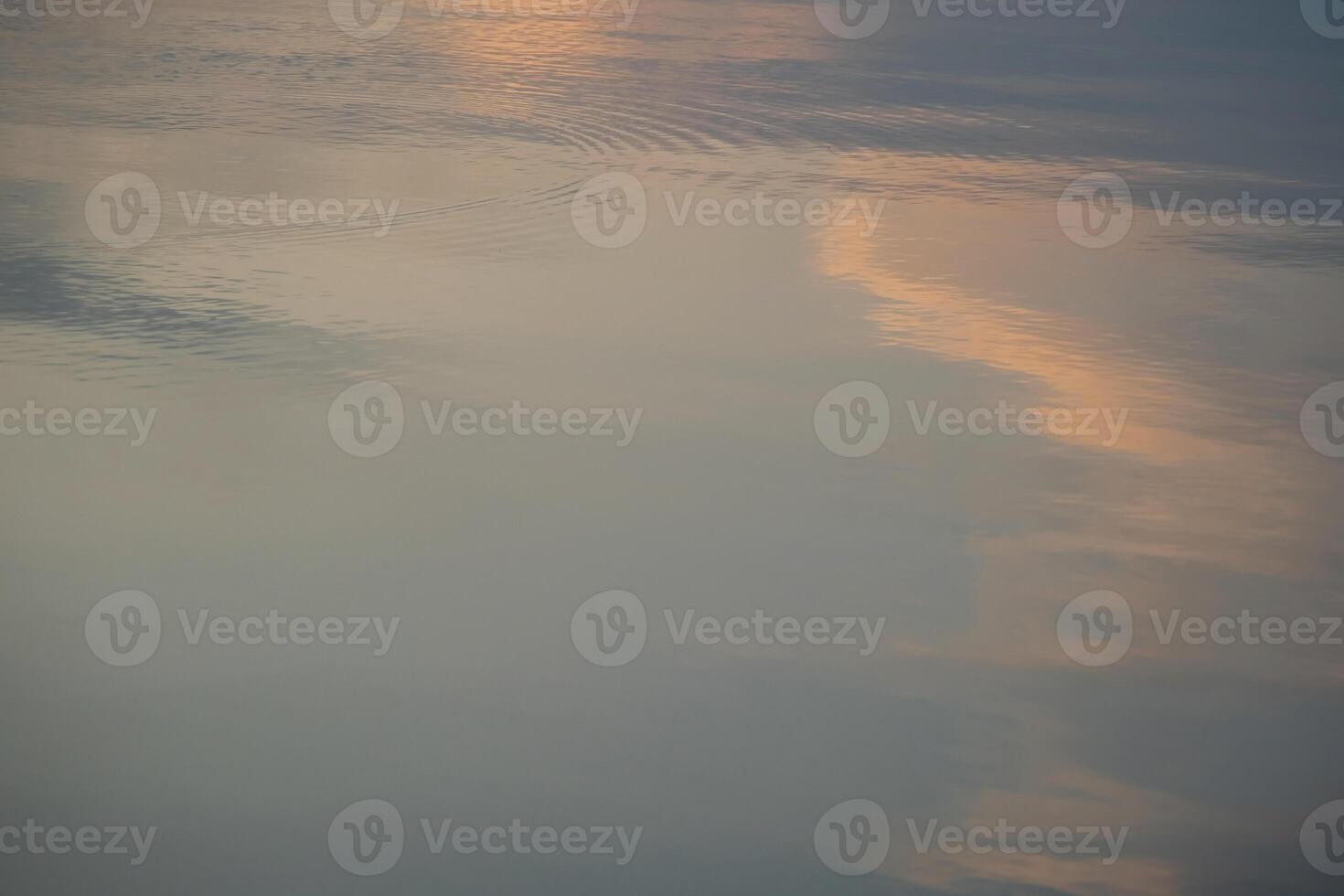 Reflection of orange sky clouds and ripples on calm lake surface during twilight photo
