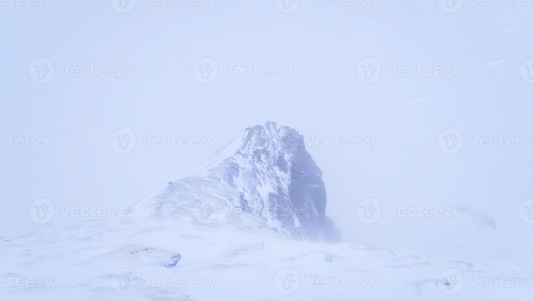 Snowy mountain peak shrouded in mist and clouds offering a sense of coldness and desolation in the winter season photo
