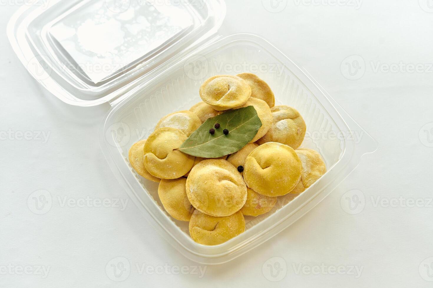 A Delicious Array of Freshly Prepared Dumplings Neatly Arranged in a Clear Plastic Container with Bay Leaves and Spices Ready for Cooking or Serving photo