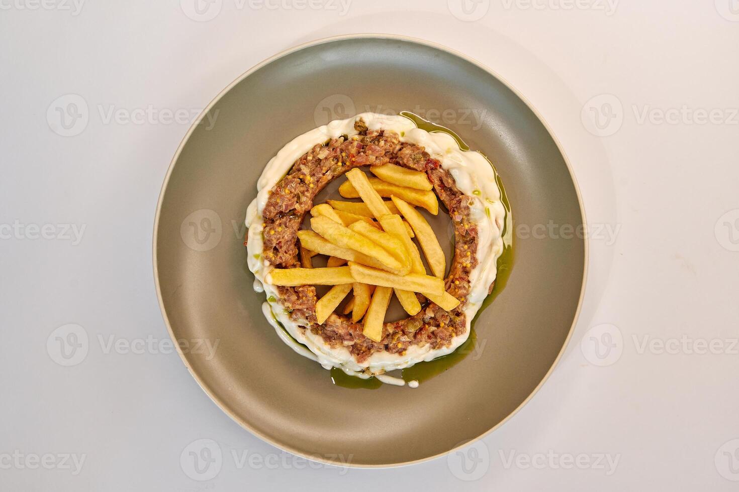 A plated dish featuring a circular arrangement of meat, surrounded by creamy sauce and topped with crispy French fries for an appetizing presentation. photo