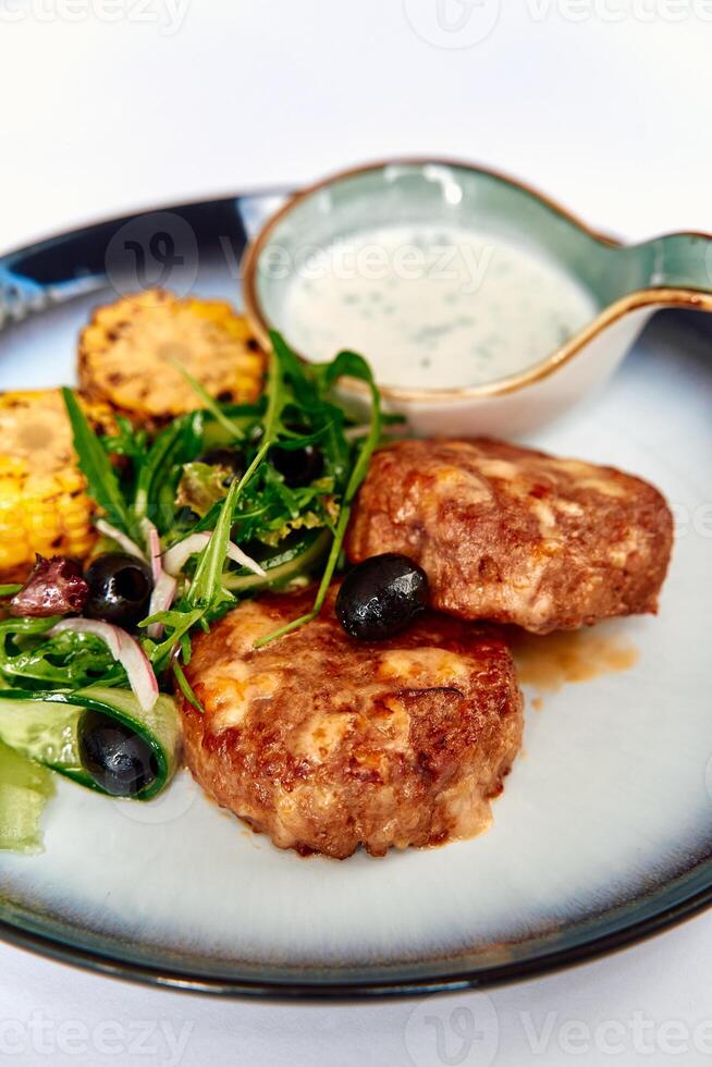 Deliciously prepared meat patties served with fresh salad and a tangy dipping sauce, showcasing vibrant colors and textures on a stylish plate photo