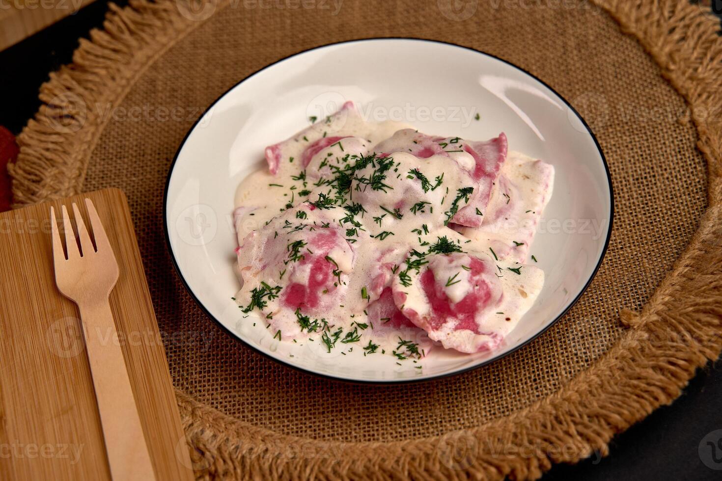 Delicious homemade ravioli served in a creamy white sauce garnished with fresh herbs on a rustic table setting designed to enhance culinary presentation. photo