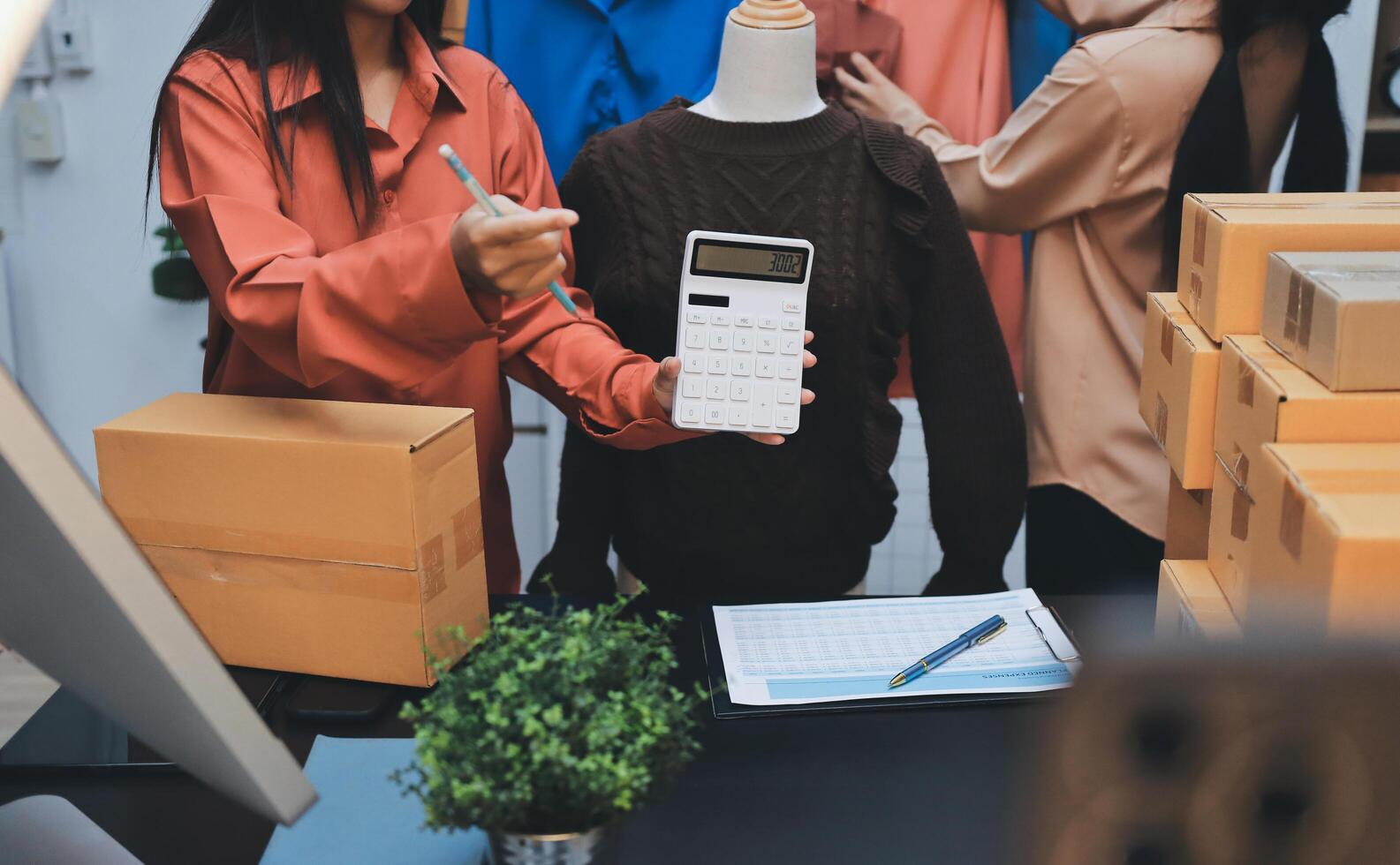 Two women are working on a computer and holding a calculator photo