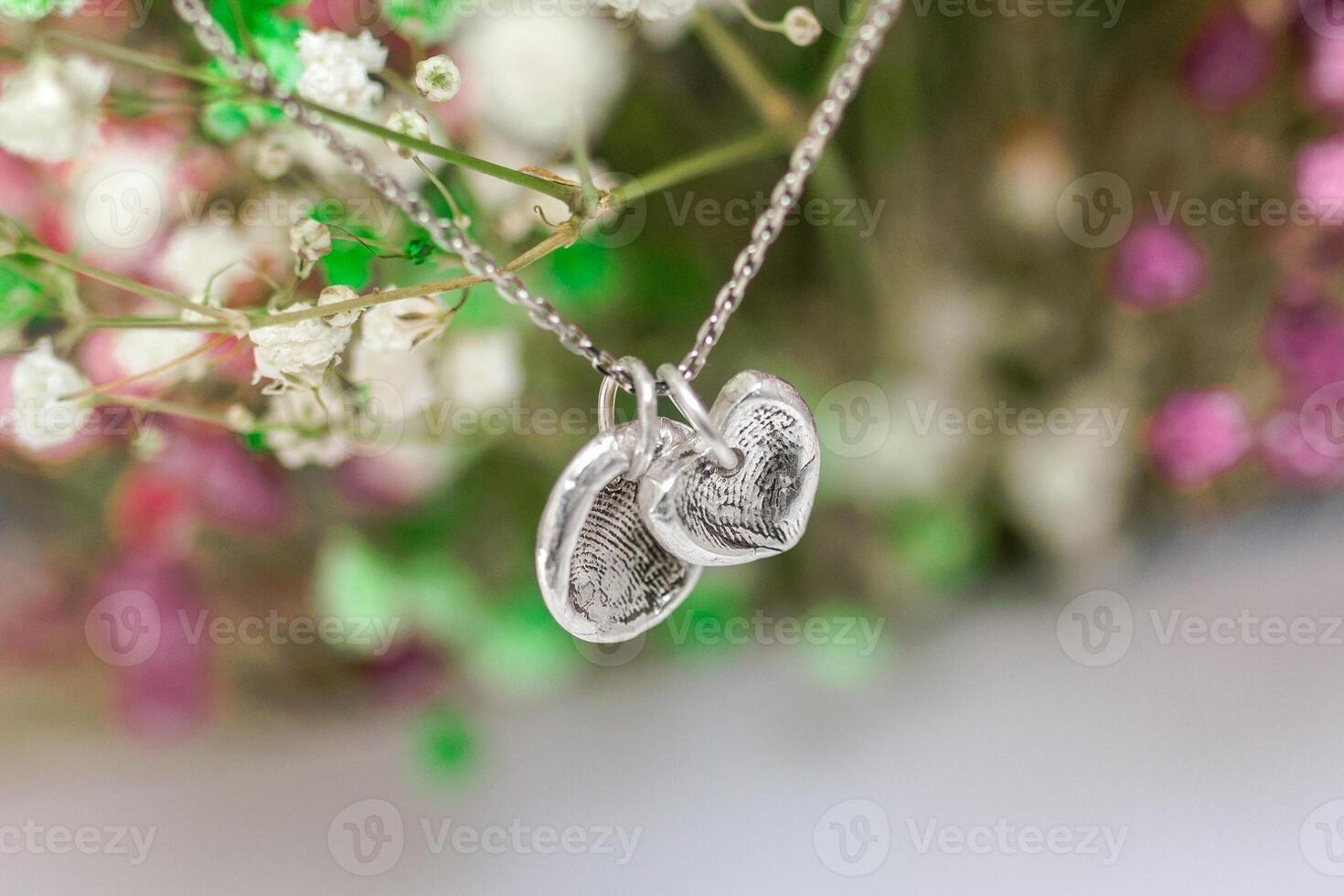 Delicate Silver Necklace with Heart and Round Pendants Featuring Fingerprint Details Amidst Flowers. photo