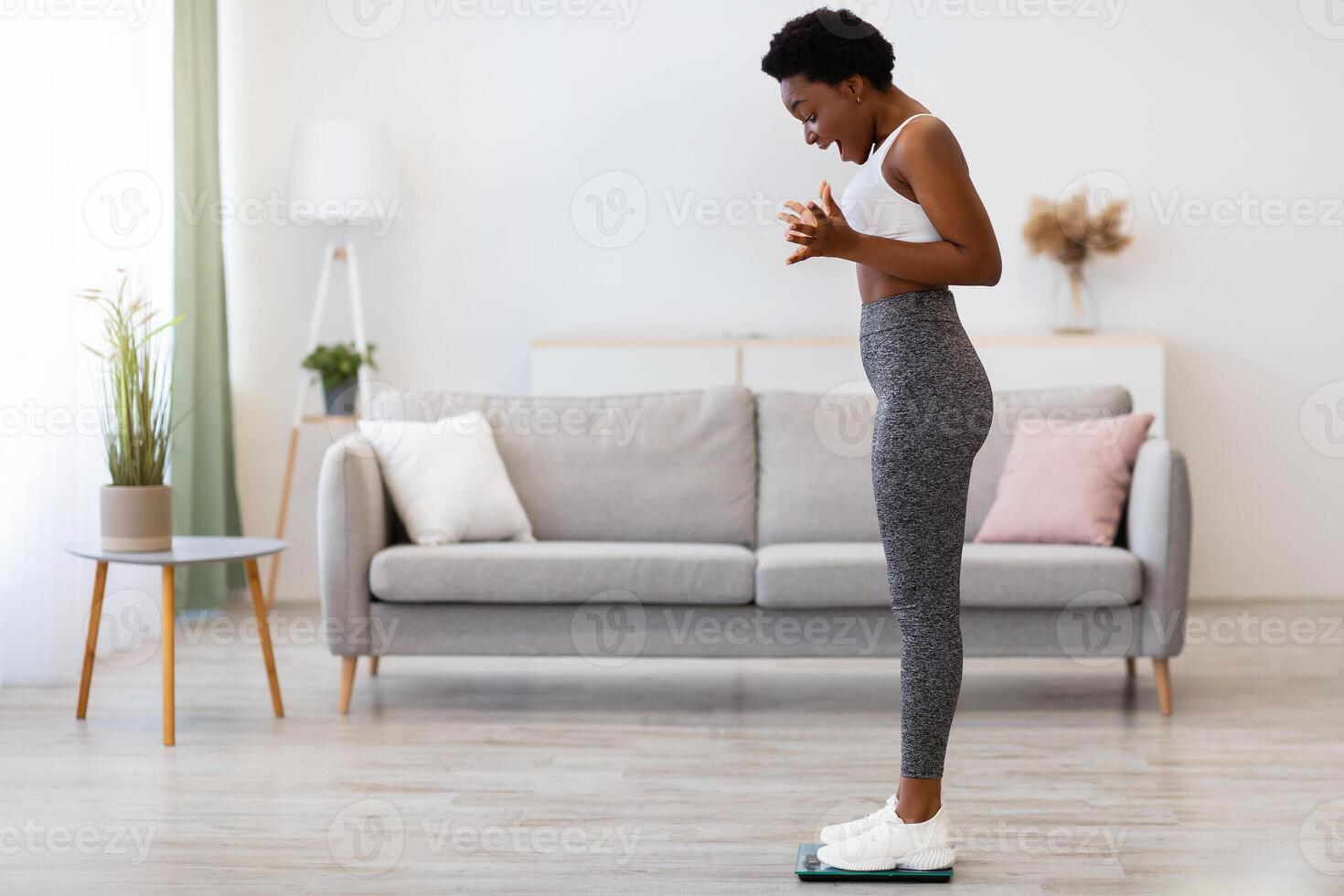 Successful Slimming. Joyful Black Lady Weighing Standing On Weight-Scales At Home And Shaking Fists In Joy. Great Weight-Loss Concept. Full Length, Side View, Empty Space For Text photo