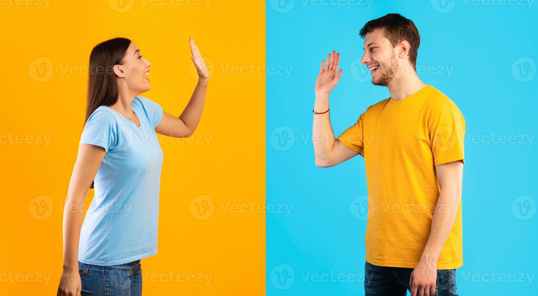 Side view profile portrait of smiling young man and woman waving to each other or giving high five standing isolated on halved yellow and blue studio background, greeting each other photo