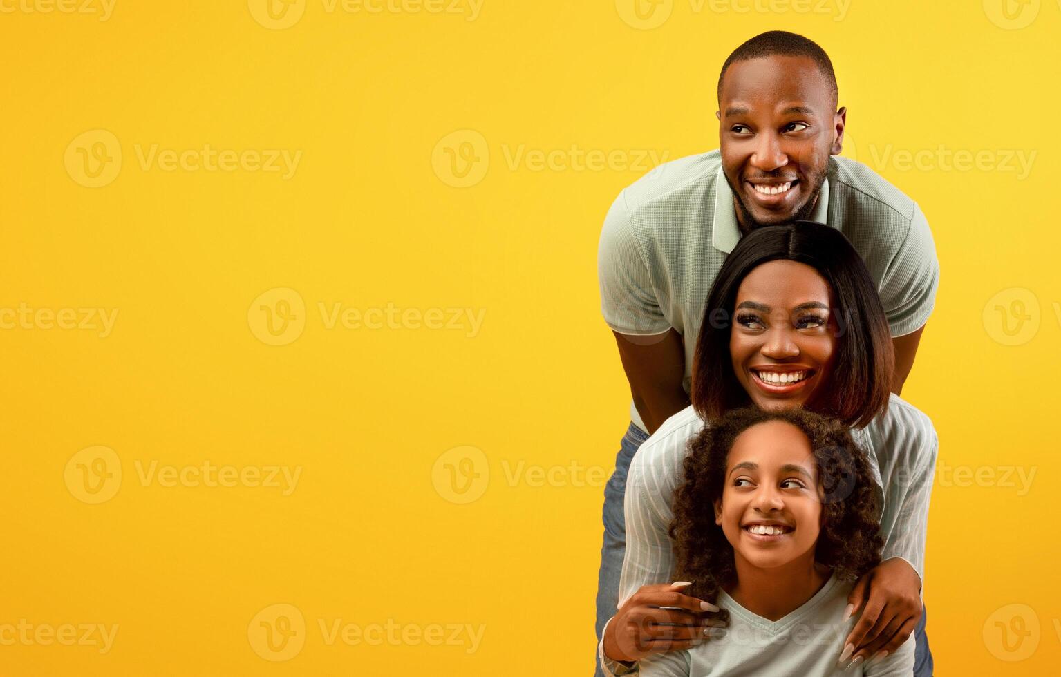 Positive african american family of three looking aside at empty space on yellow studio background, standing behind each other. Look there, promo and cool offer concept. Free space for advertisement photo