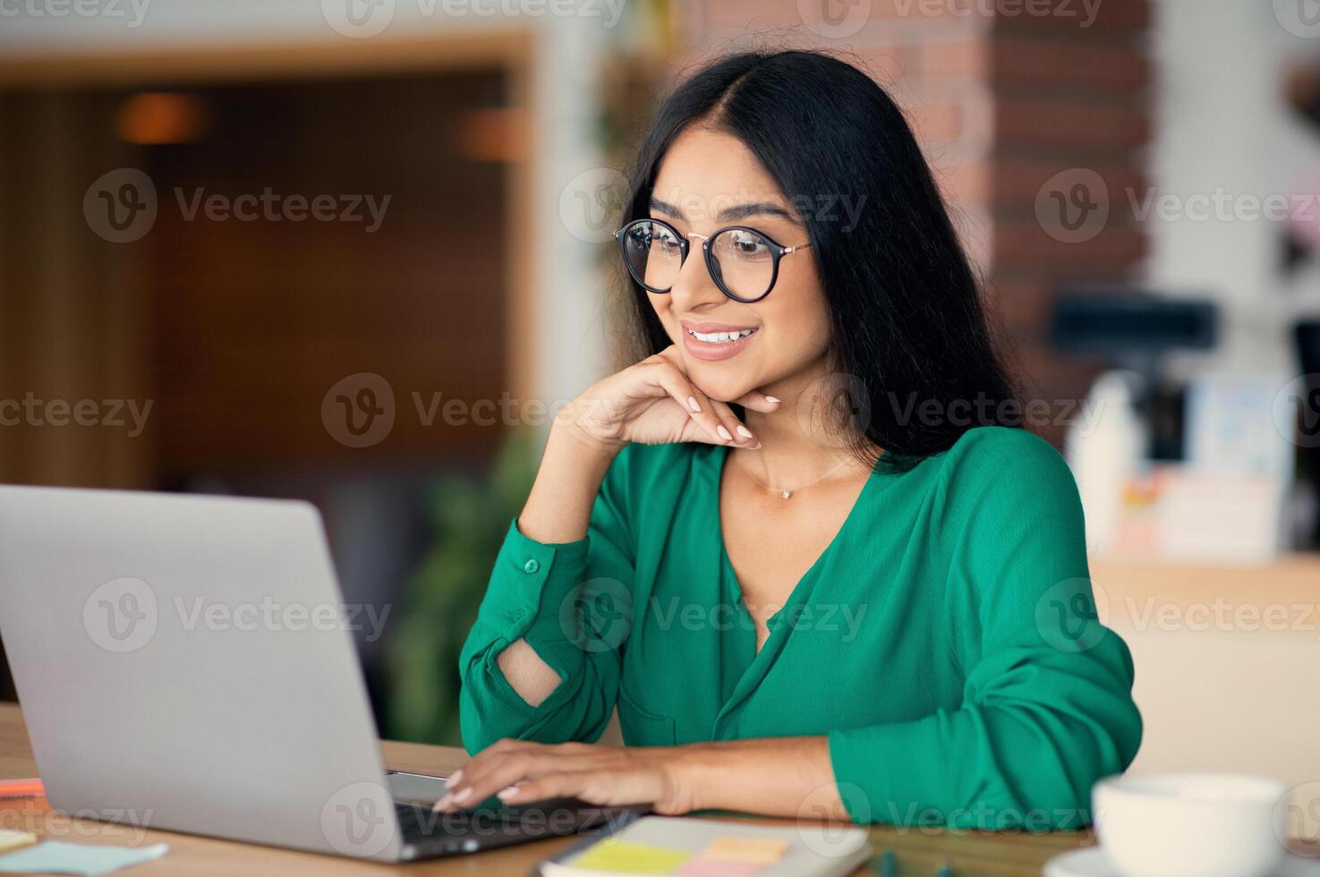 Attractive young indian woman studying or working online at cafe, cheerful arabic millennial lady typing on notebook keyboard, surfing on Internet while coffee break, using laptop, empty space photo