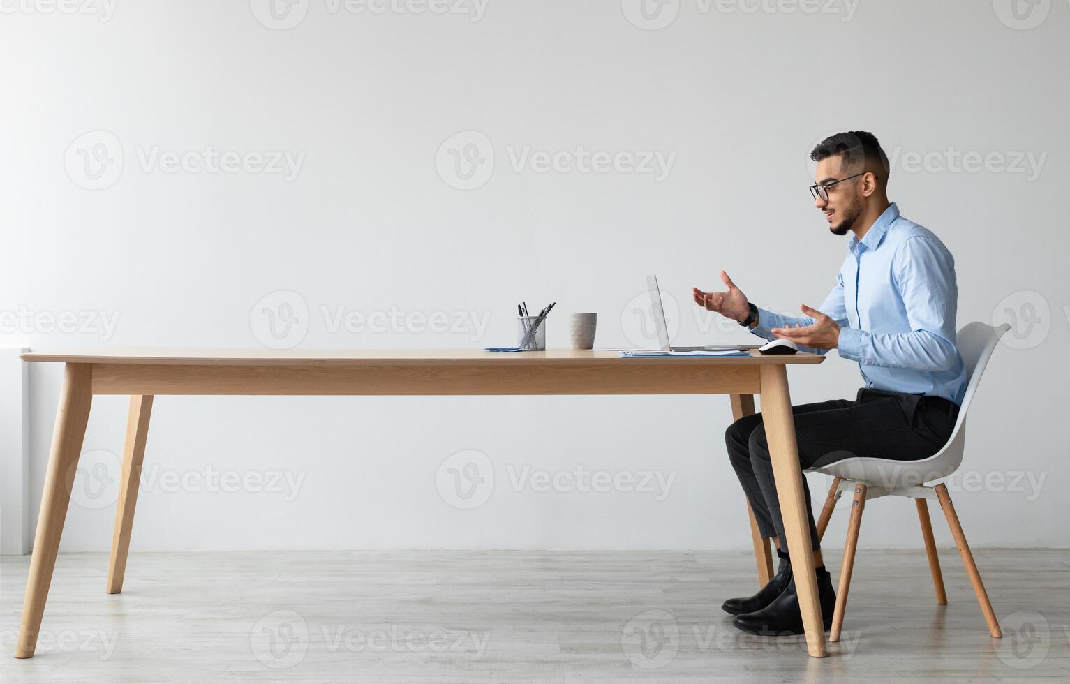 Conference. Profile side view portrait of Middle Eastern businessman in glasses having web call using laptop sitting at desk at workplace, talking and gesturing at webcam, free copy space banner photo