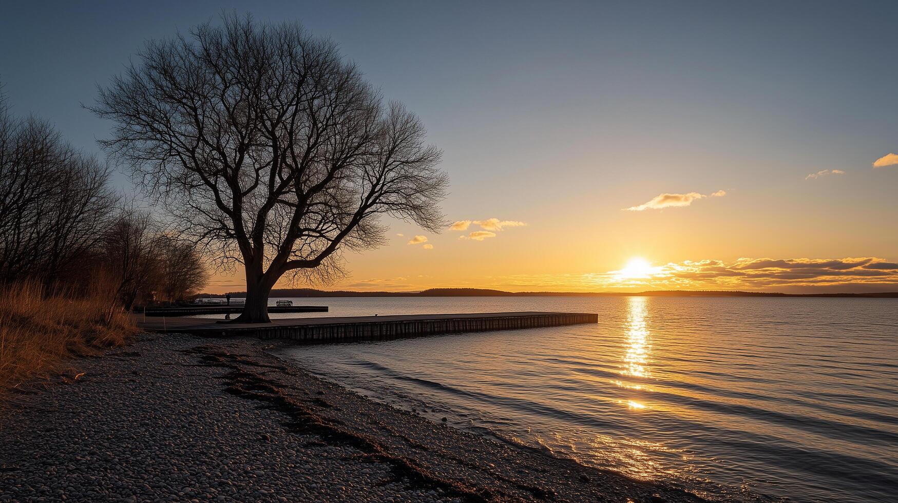 Sunset over the water of a calm lake, with a dock, trees, and a sandy beach photo