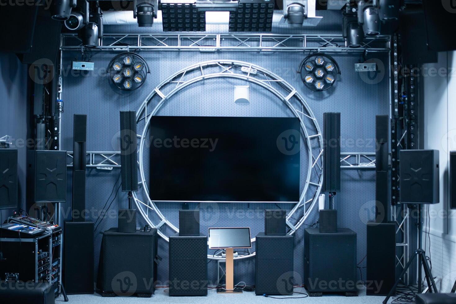 A high-tech room with a sound system around and a large display in the center. Stylish and modern technology for watching movies. Audio speakers, lights and other home and studio amenities. photo