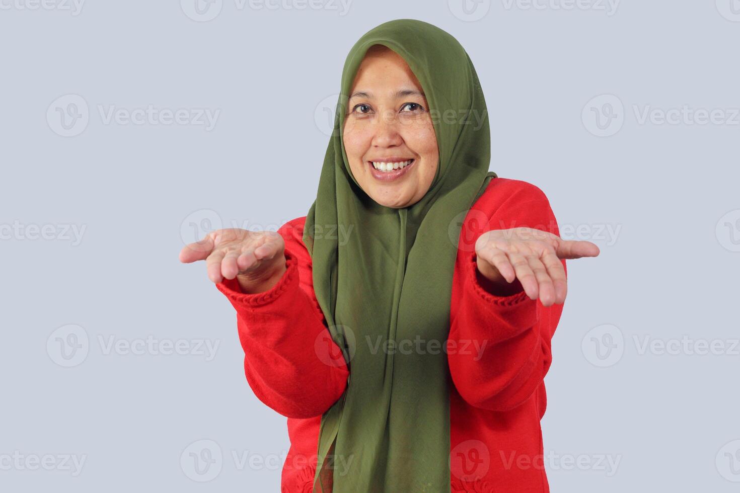Portrait of cheerful hijab woman smiling and showing open palms forward, welcoming and inviting expression, isolated studio shot for campaign or support themes photo