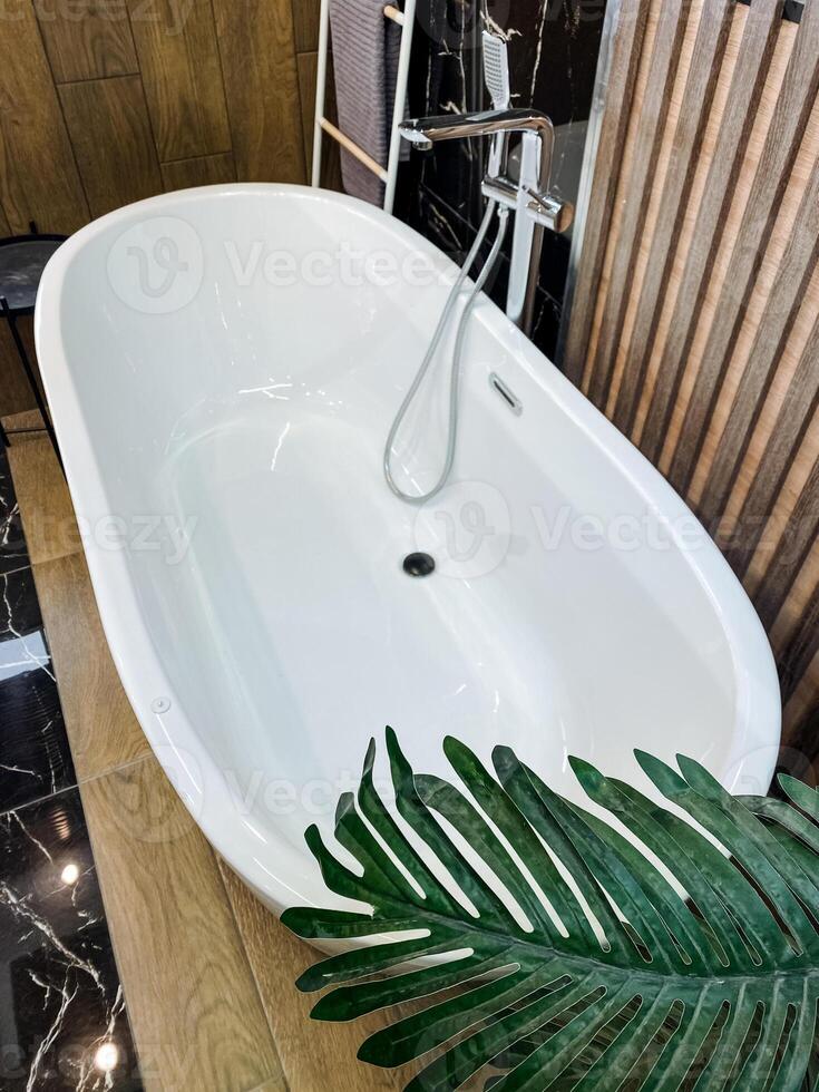 In a beautifully designed bathroom, a pristine white bathtub is elegantly placed on a smooth wooden counter, complemented by a vibrant palm tree leaf that adds a touch of nature photo