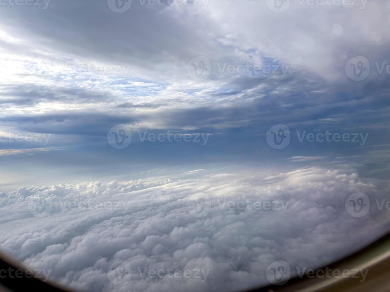 Looking out from an airplane above a swirling sea of clouds and a radiant sky. An atmospheric airplane view above dense clouds. Scenic or business flight travel photo. Nature background. photo
