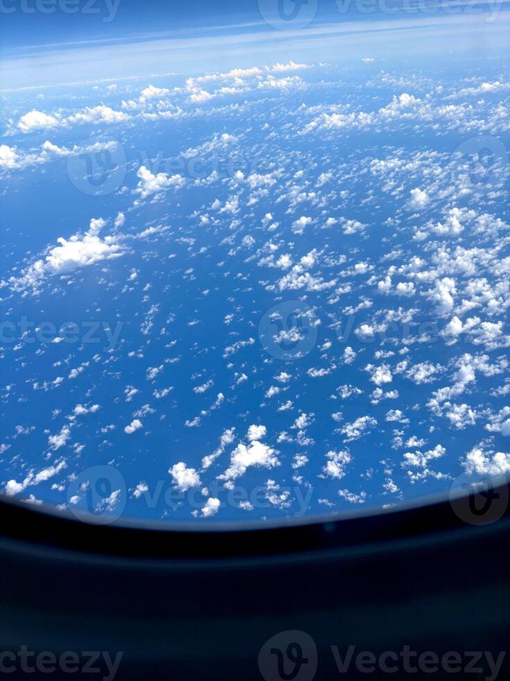 An aerial view captured from an airplane window. Puffy white clouds scatter across a deep blue sky, floating above the sea below. The image captures the nature of vast Pacific Ocean seen from above. photo