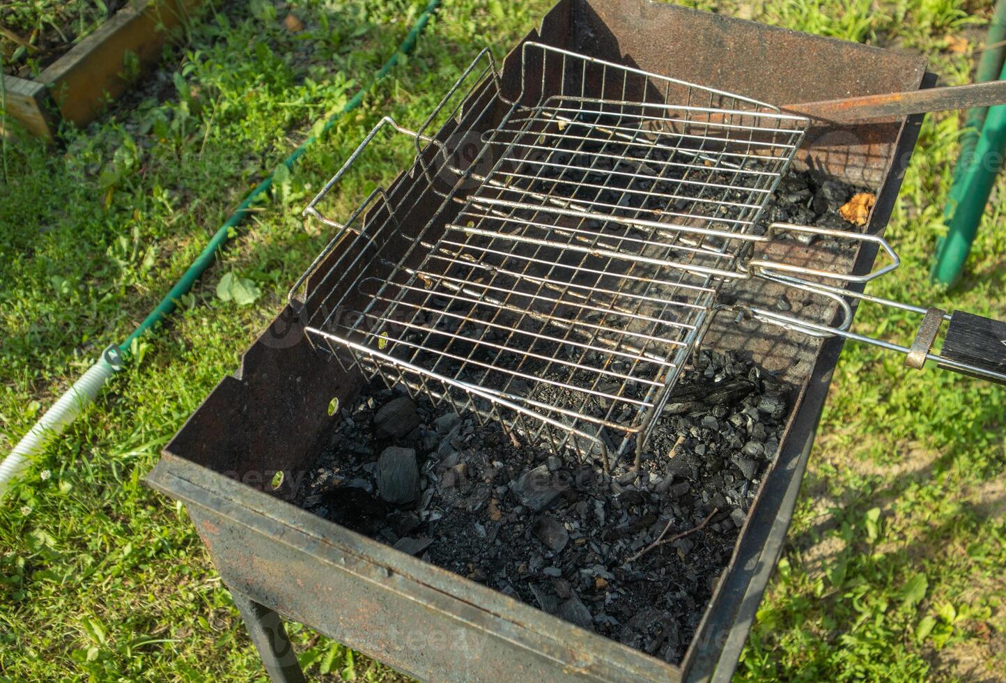 An overhead view of a metal charcoal grill and grill grate against a backdrop of green grass photo