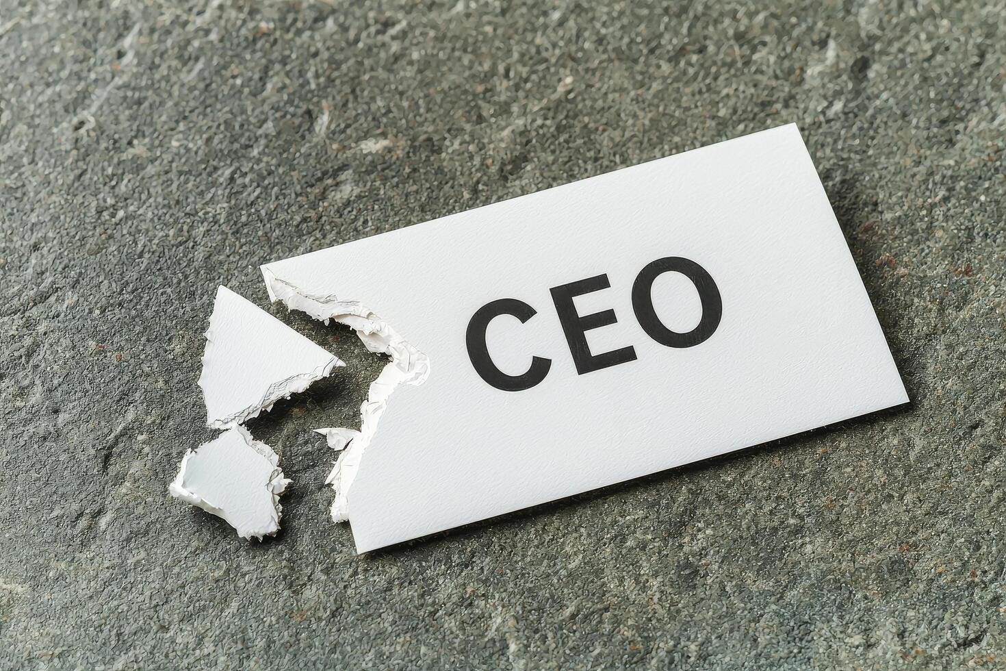 Torn white business card with CEO text lying on rough gray surface, symbolizing broken leadership or lost authority photo