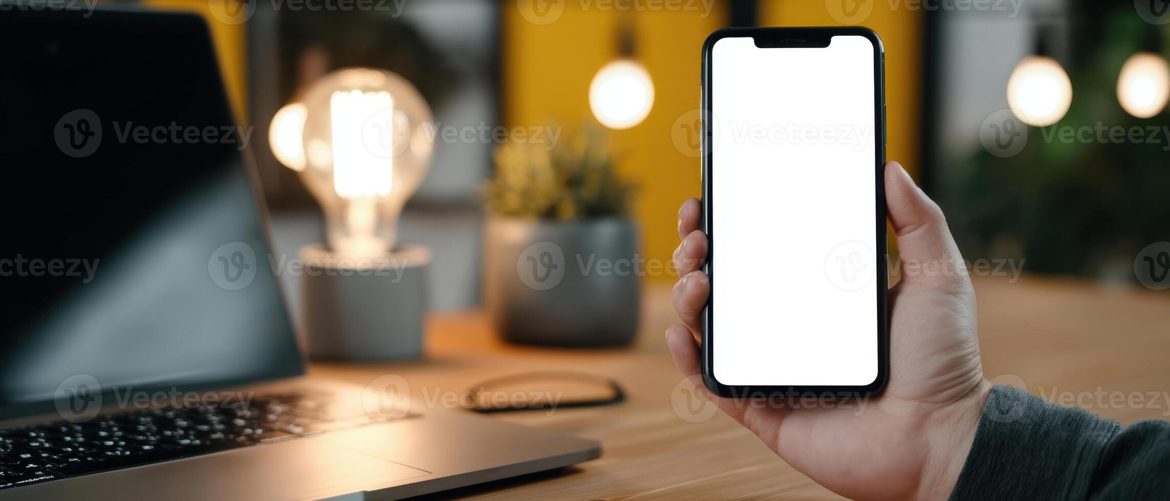 The smartphone being held in hand with a blank screen in a cozy workspace. photo