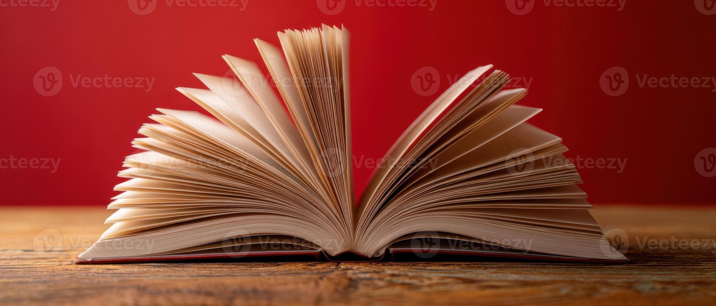 The open book resting on a wooden table with a vibrant red background. photo