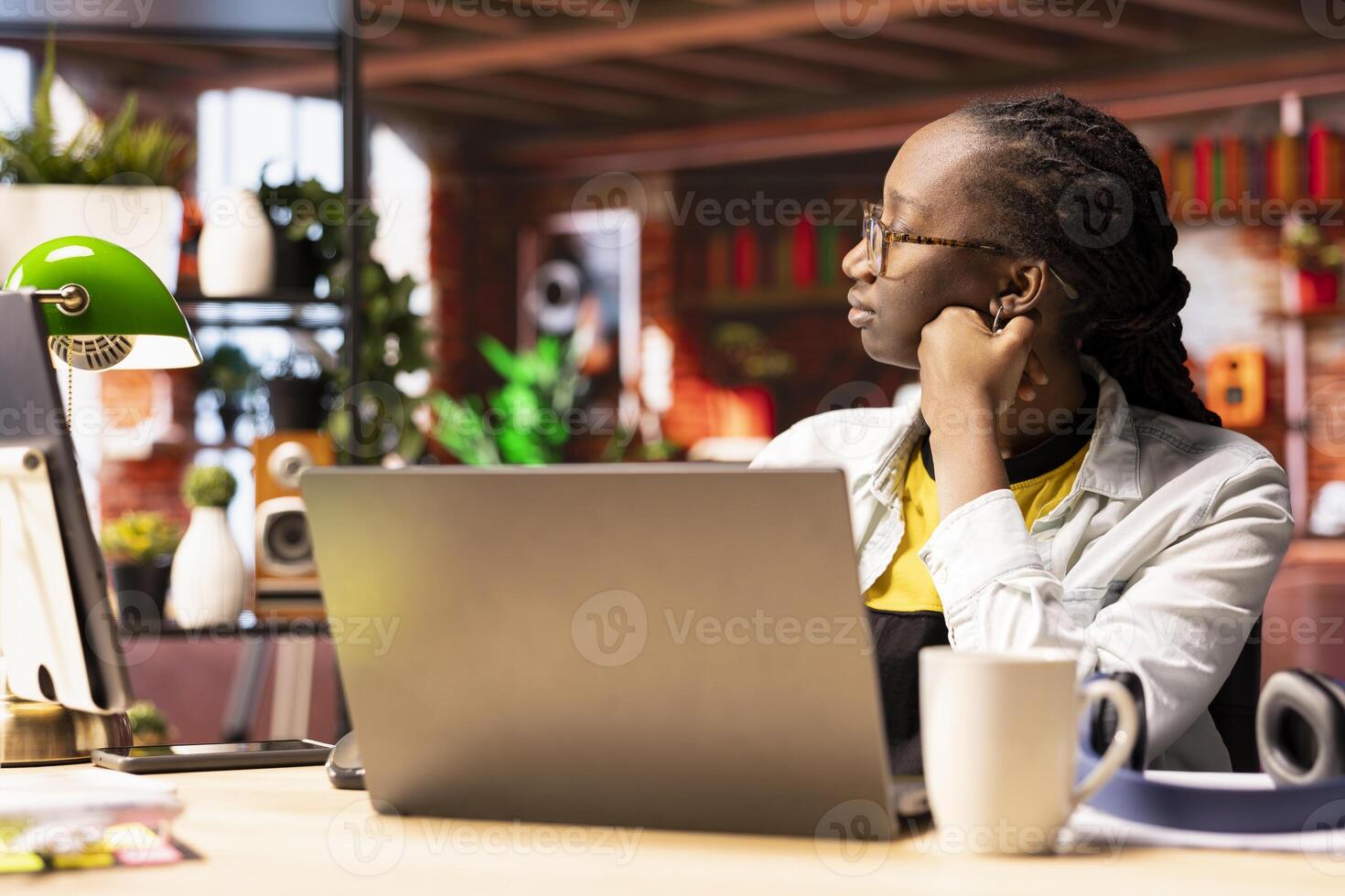 Remote worker pausing work done on laptop at home to pensive thinking. African american teleworker in apartment feeling bored by repetitive tasks, stopping work on notebook to daydream photo
